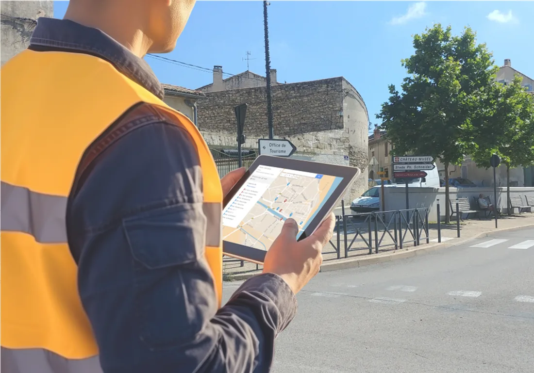 Technicien en gilet jaune qui relève un défaut sur une tablette, dans une rue
